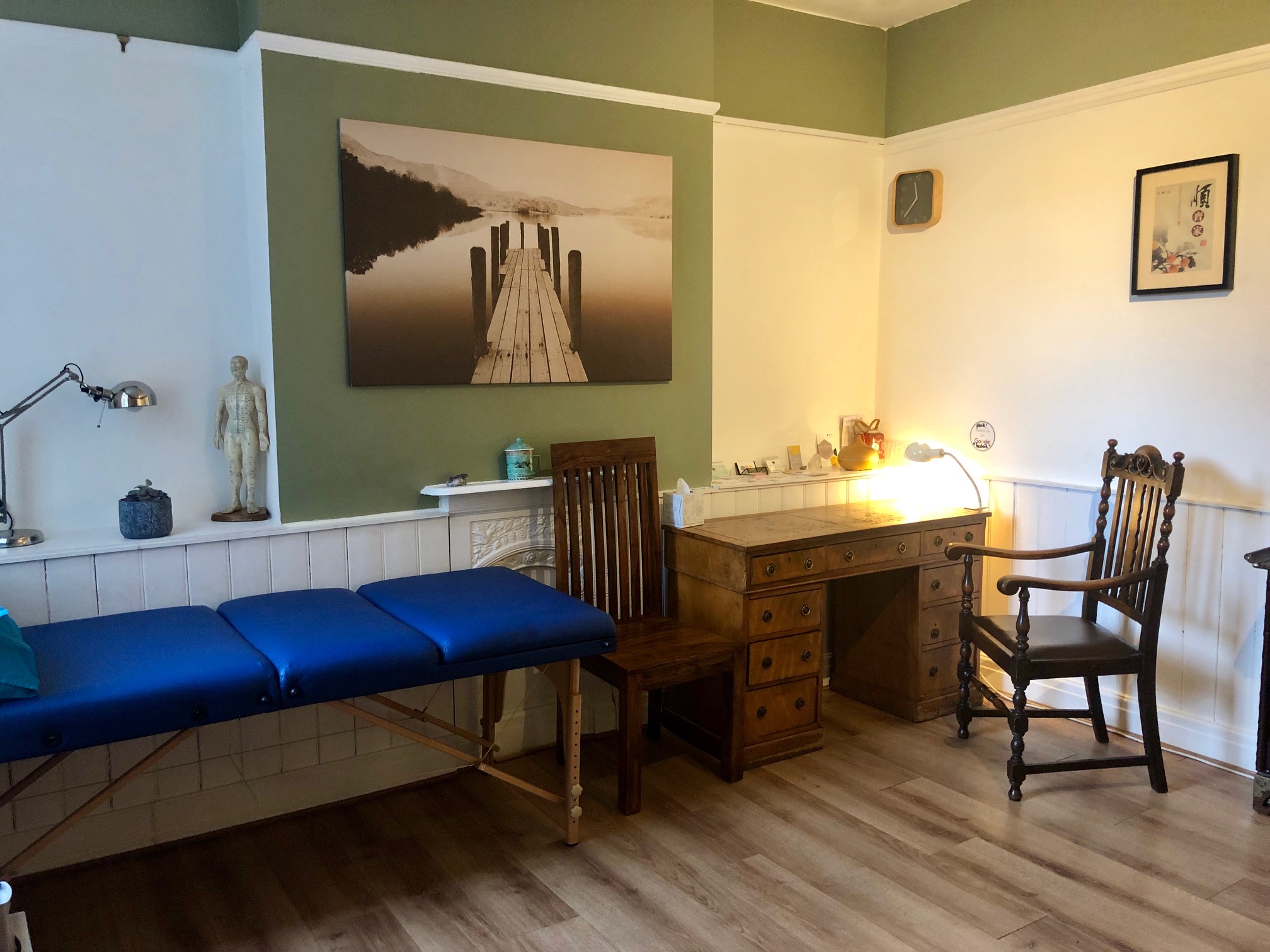 One side of the room with a desk, two wooden chairs and the edge of the massage table
